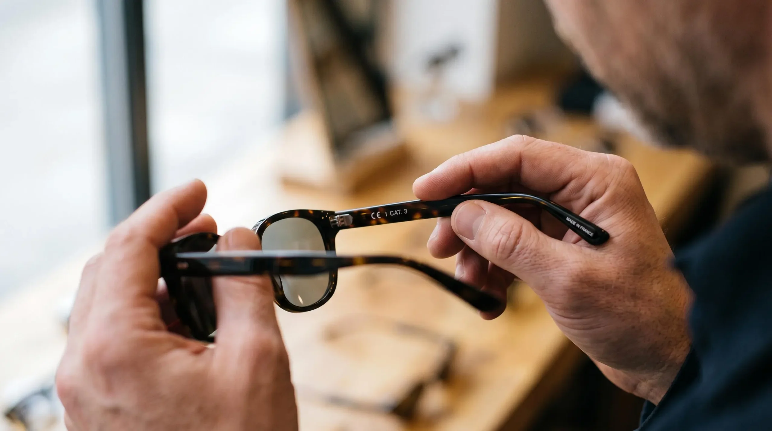 Gros plan sur des mains lisant le marquage CE et la catégorie de filtre gravés à l'intérieur d'une branche de lunettes de soleil.